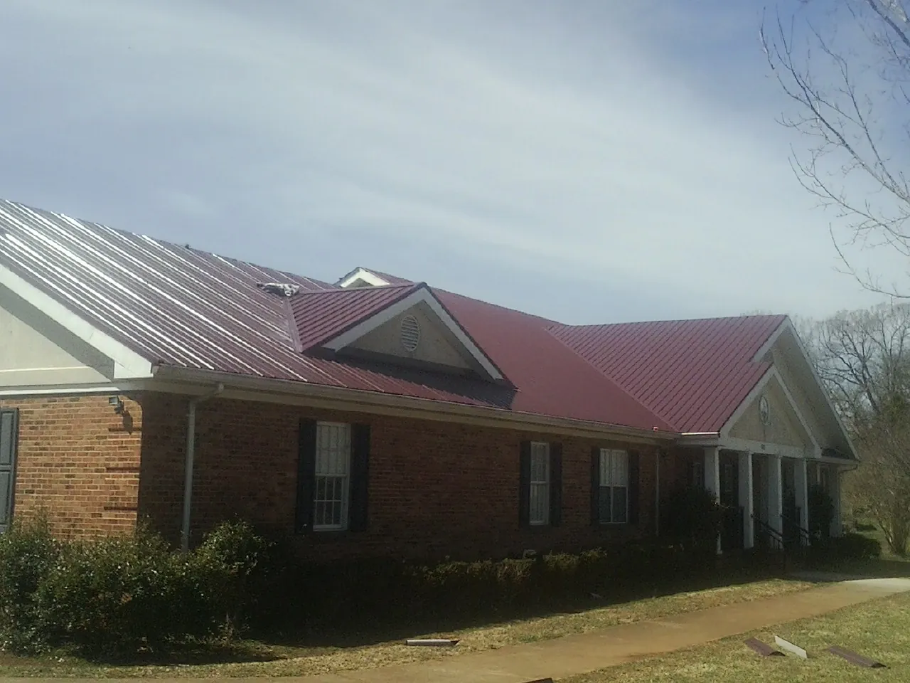 Red metal roof with gabled entries on a long brick building, from a Hail Damage Roof Repair job in Manti