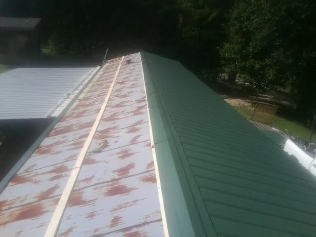 Old rusted panels beside newly installed green metal roofing — Wind Damage Roof Repair by Roofing Brothers in Manti