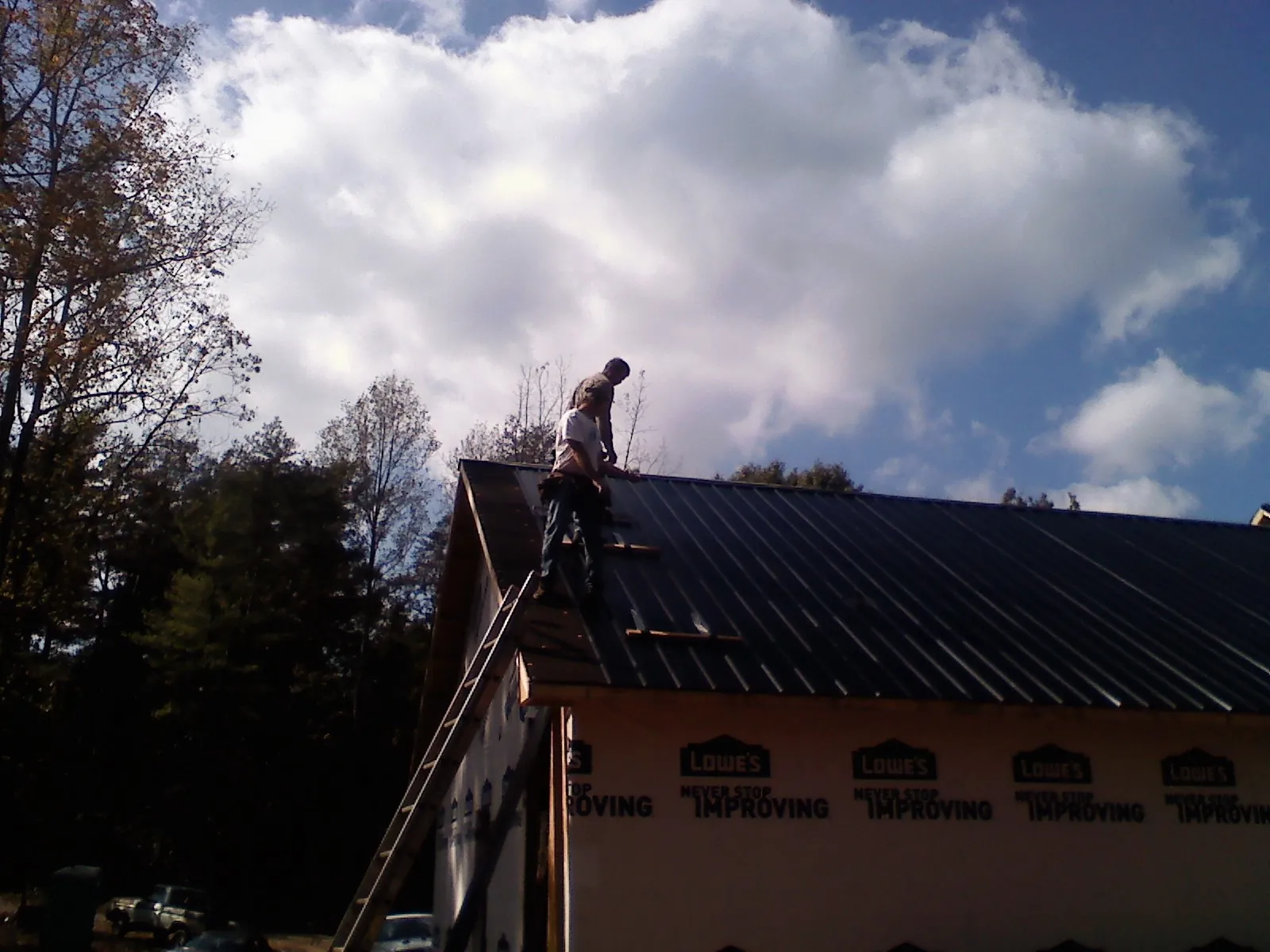 Roofer fastening dark metal panels high against a cloudy sky, from a Roof Inspection job in Manti