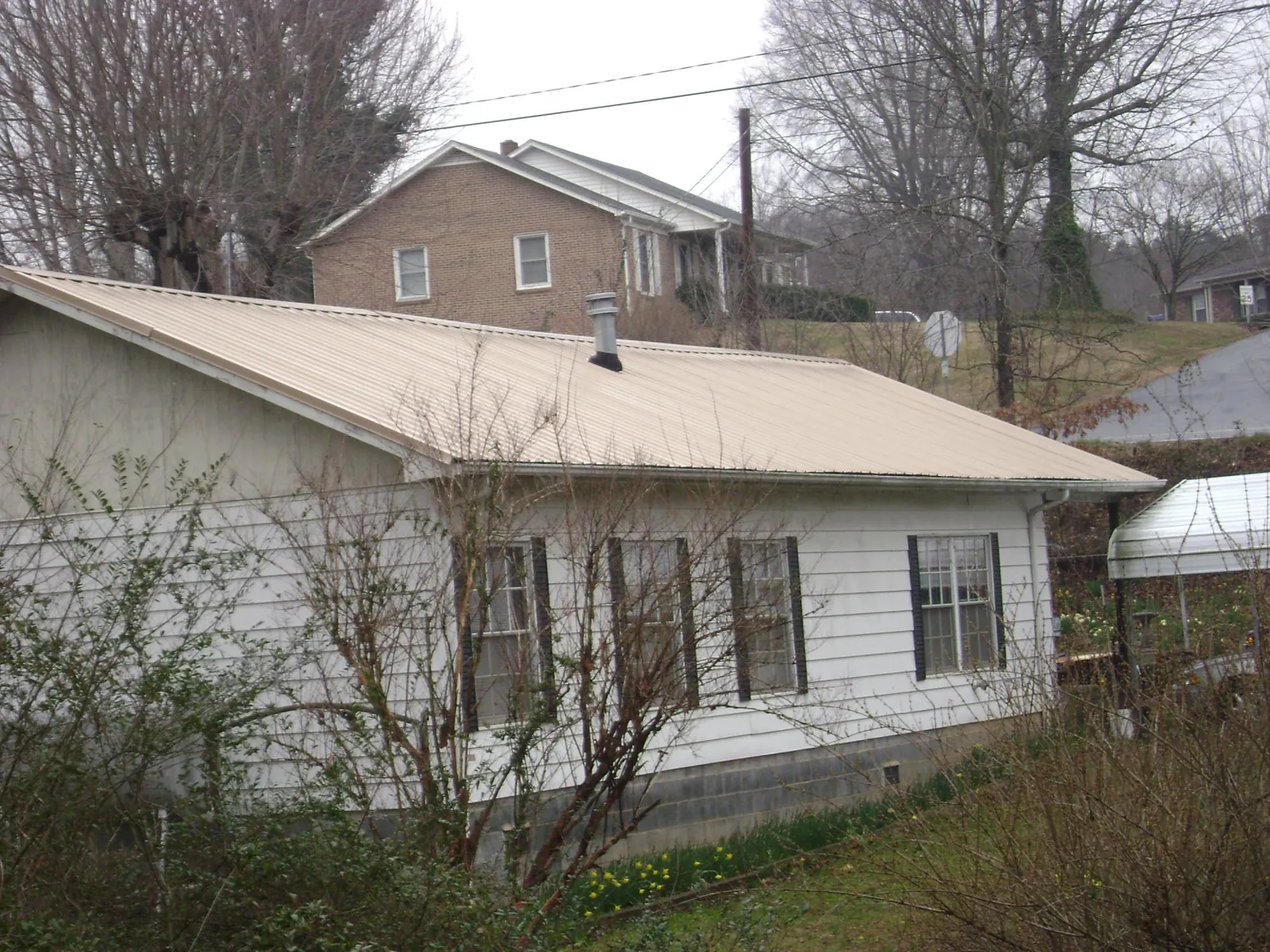 Tan metal roof on a white sided house set into a hillside — Commercial Roofing by Roofing Brothers in Manti